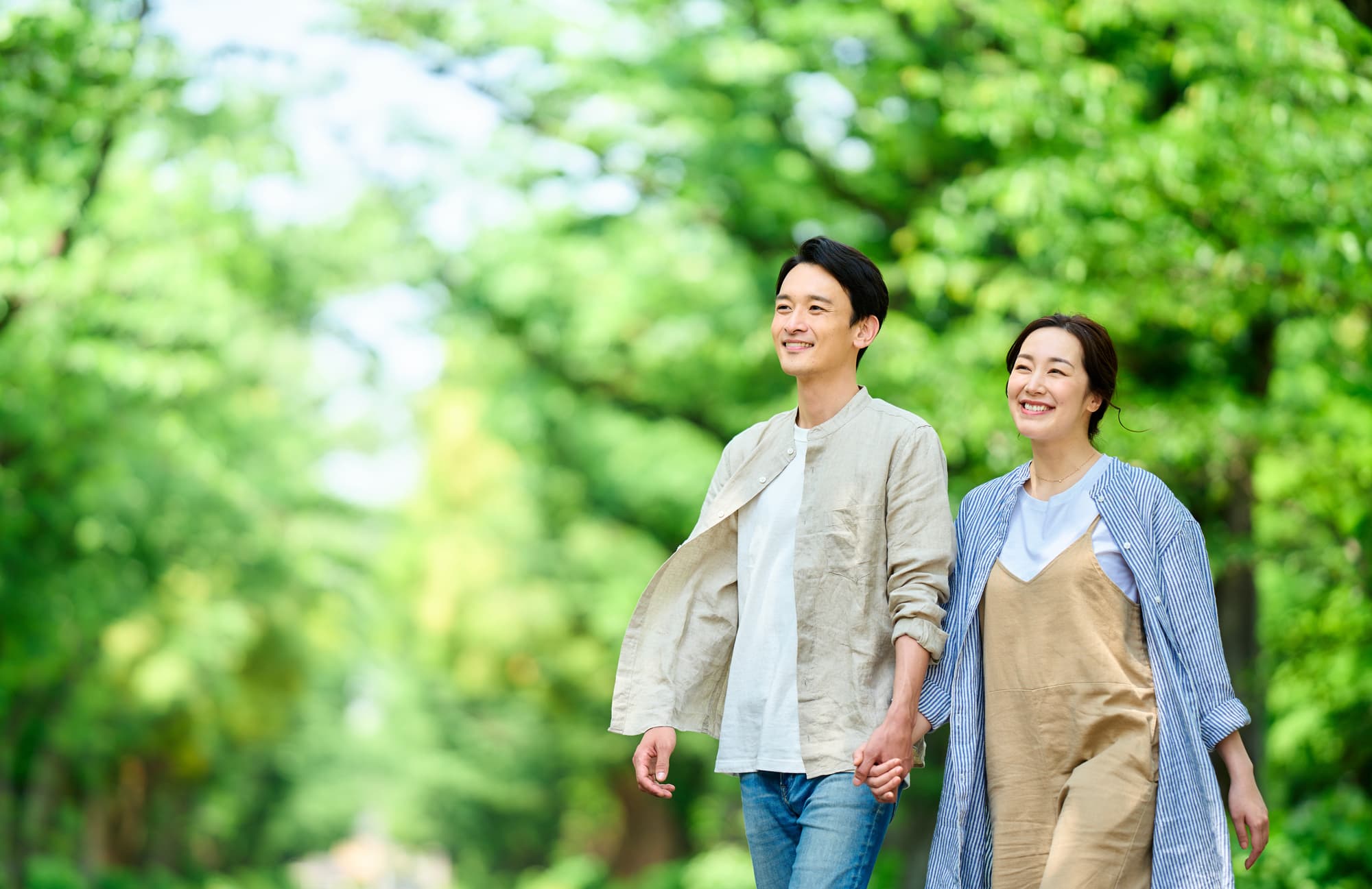 新緑の中を手を繋ぎ歩く男女