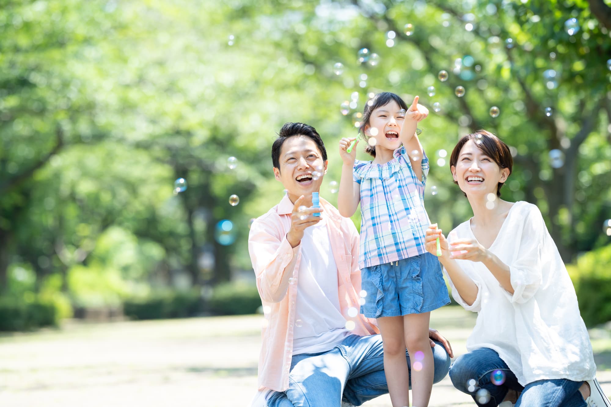 公園でシャボン玉遊びをする子どもと笑顔で見守る両親